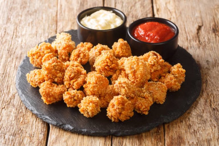 A slate platter with Crunchy Chicken Dippers, served alongside two small bowls of dipping sauces—one creamy and one red—on a wooden table.