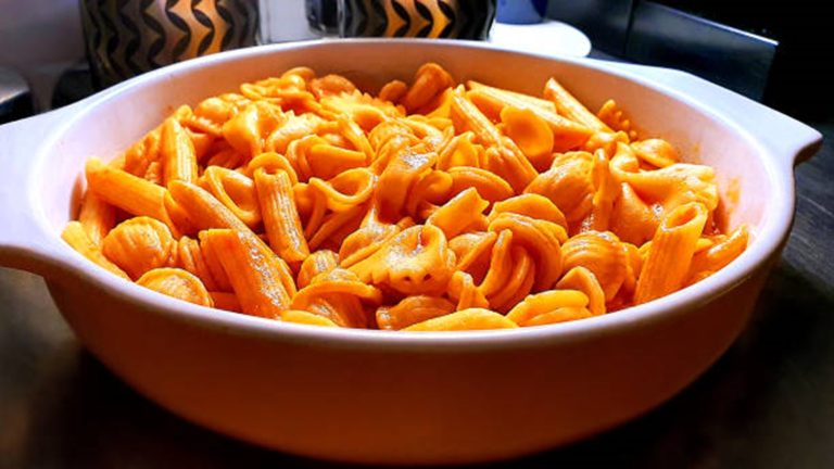 A white dish filled with Hidden Veggie Pasta—penne and orecchiette coated in a red-orange sauce—sits on a dark surface.