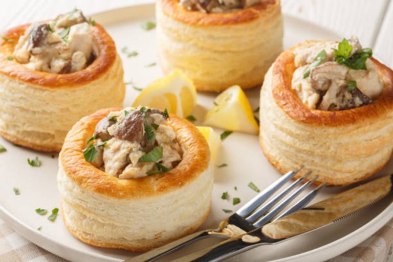 Four puff pastry Mini Chicken Pies filled with creamy mushroom, chicken and sweetcorn, garnished with herbs, are served on a white plate with lemon wedges and cutlery.
