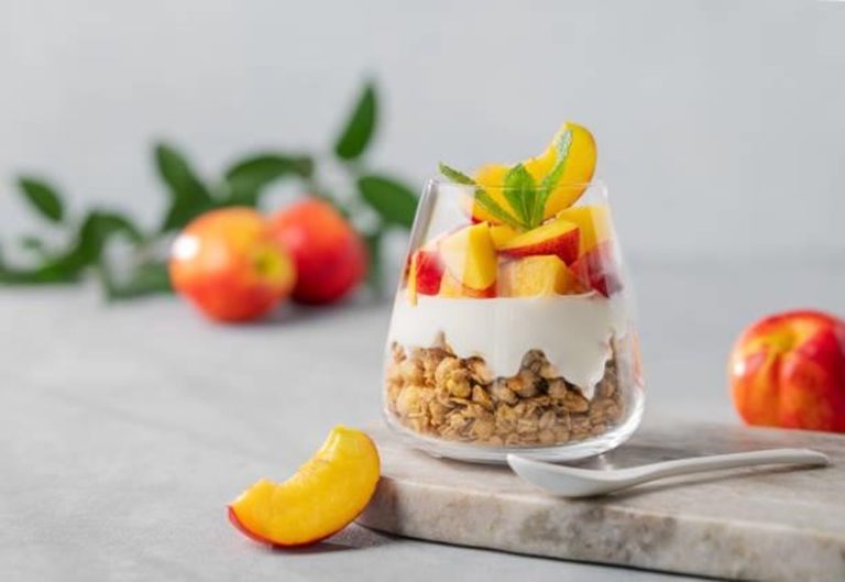 Layered peachy parfait cups with creamy yogurt, granola, and fresh peaches in a glass.