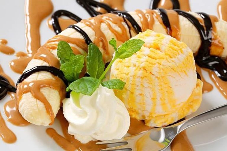A tall glass of creamy banana caramel swirl milkshake topped with whipped cream, caramel drizzle, and banana slices.”