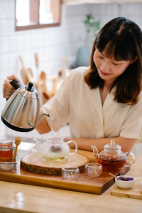 A steaming cup of soursop leaf tea with fresh green soursop leaves on a wooden table.